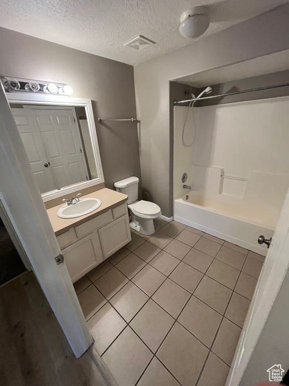Full bath featuring vanity, toilet, shower / tub combination, tile patterned floors, and a textured ceiling