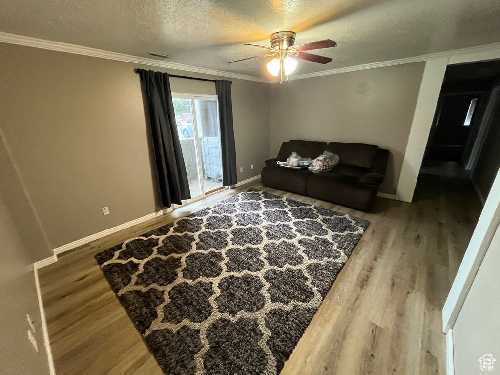 Living area featuring wood finished floors, ornamental molding, baseboards, a ceiling fan, and a textured ceiling