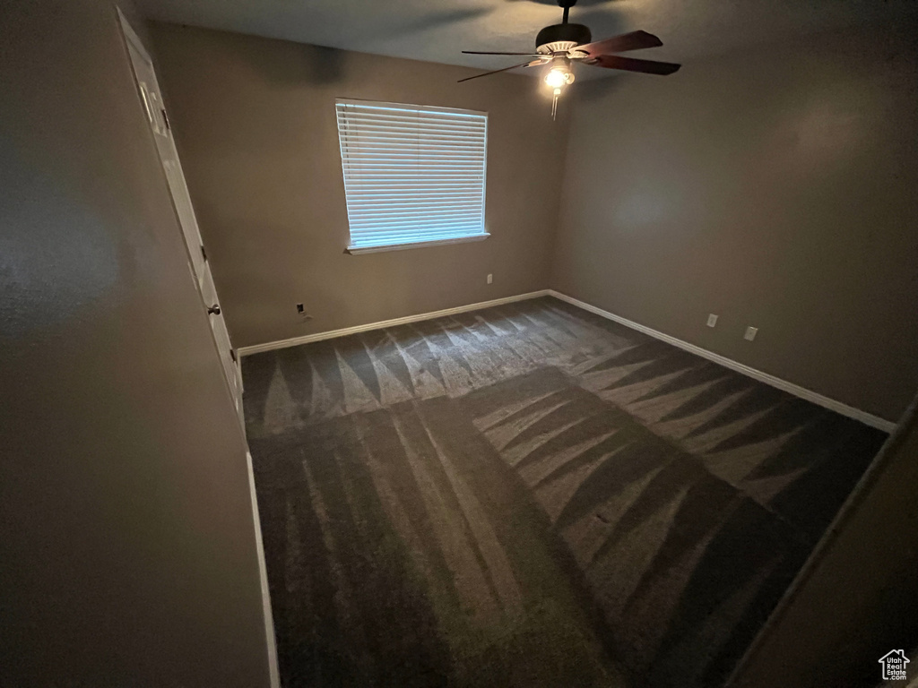 Unfurnished room featuring baseboards, dark carpet, and ceiling fan