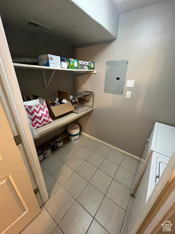 Laundry area featuring electric panel, tile patterned flooring, baseboards, and washing machine and clothes dryer