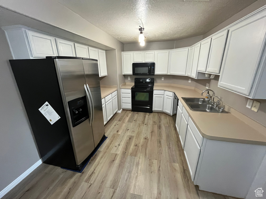 Kitchen with black appliances, a sink, light wood-style flooring, a textured ceiling, and light countertops