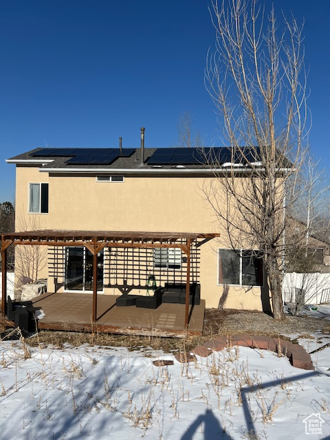 Snow covered rear of property featuring stucco siding, solar panels, and a pergola