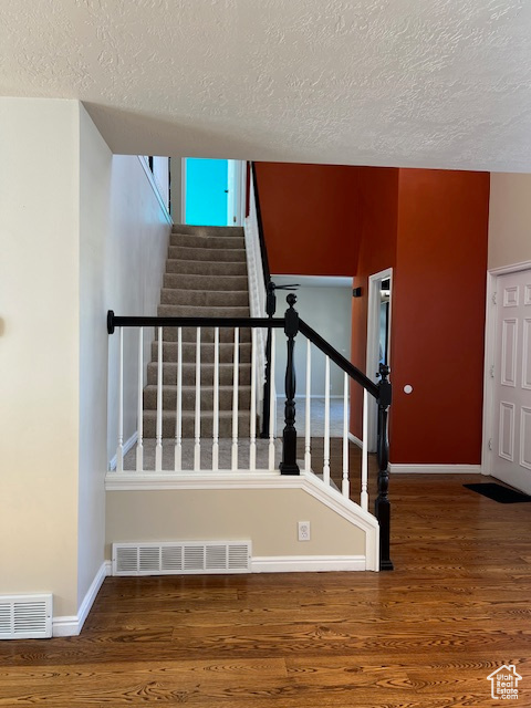 Stairs featuring a textured ceiling, wood finished floors, and baseboards