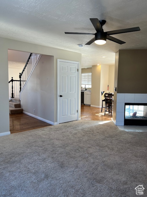 Unfurnished living room with carpet floors, a ceiling fan, baseboards, a textured ceiling, and a fireplace