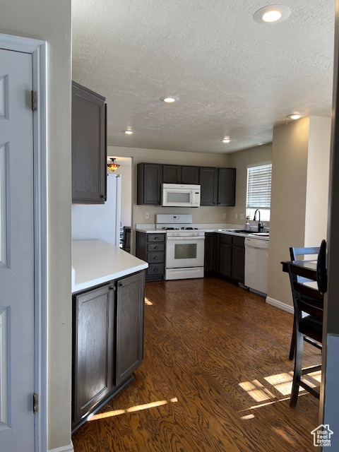 Kitchen with white appliances, a textured ceiling, dark wood-style flooring, light countertops, and recessed lighting