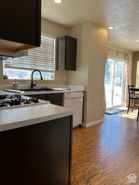 Kitchen featuring white appliances, a textured ceiling, light wood finished floors, a sink, and light countertops