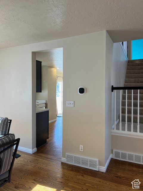 Hallway featuring wood finished floors, a textured ceiling, baseboards, and stairway