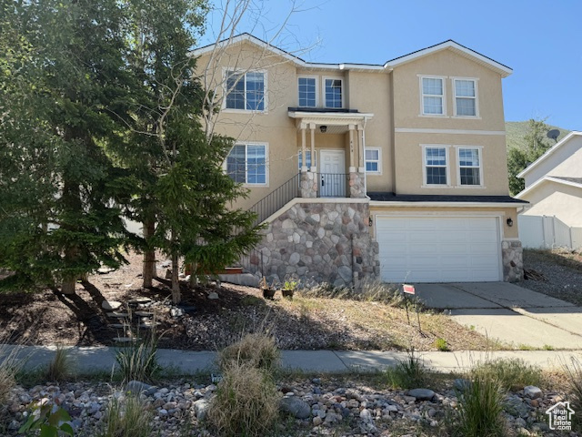 View of front of house featuring concrete driveway, an attached garage, stone siding, and stucco siding