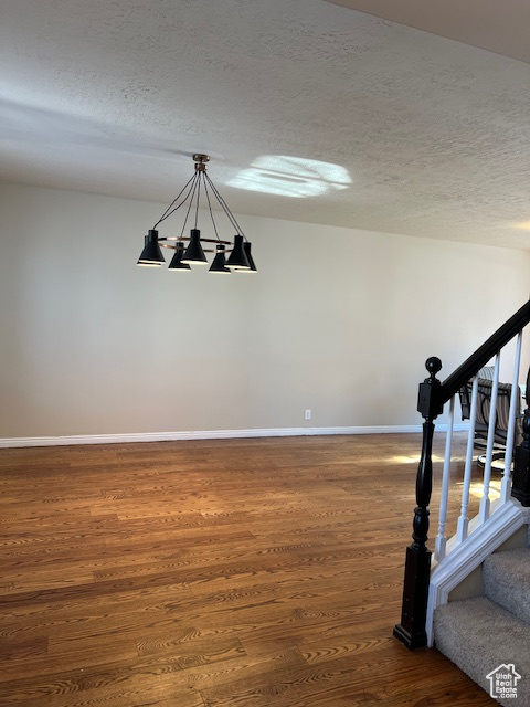 Stairs featuring wood finished floors, a chandelier, baseboards, and a textured ceiling