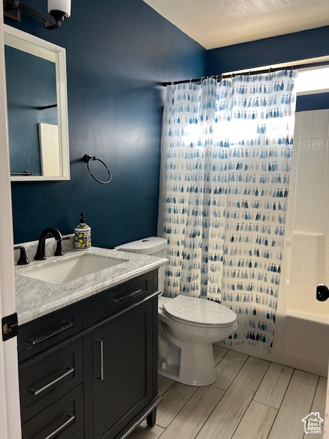 Bathroom with vanity, a textured ceiling, toilet, shower / bath combination with curtain, and wood finish floors