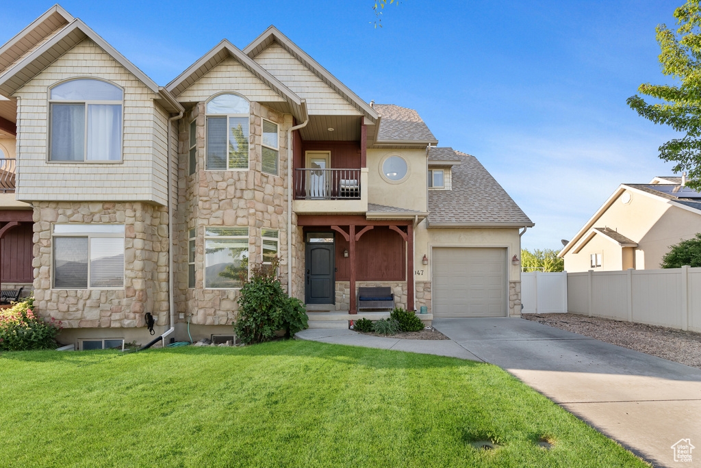 View of front of home with stone siding, a balcony, driveway, and a garage