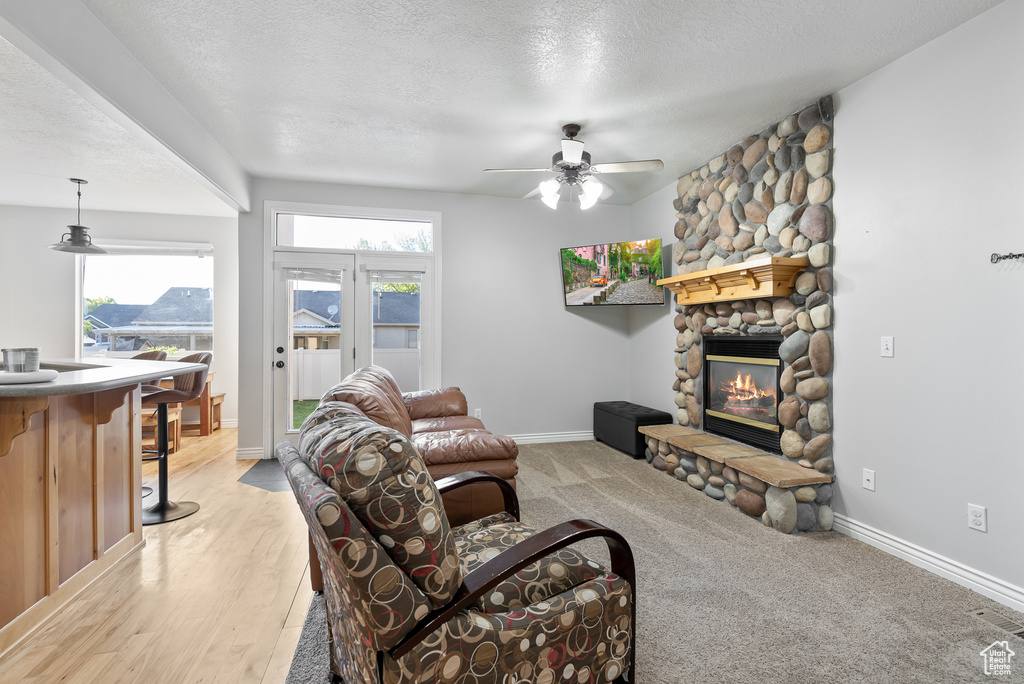Living area with ceiling fan, healthy amount of natural light, a fireplace, a textured ceiling, and baseboards