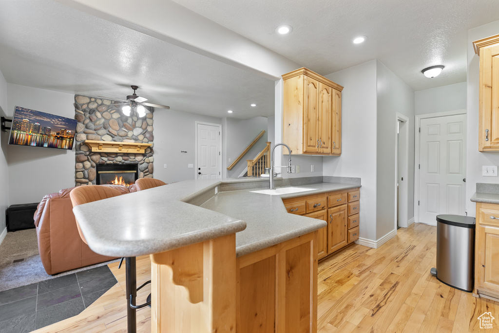 Kitchen featuring a sink, ceiling fan, a peninsula, a fireplace, and a kitchen bar