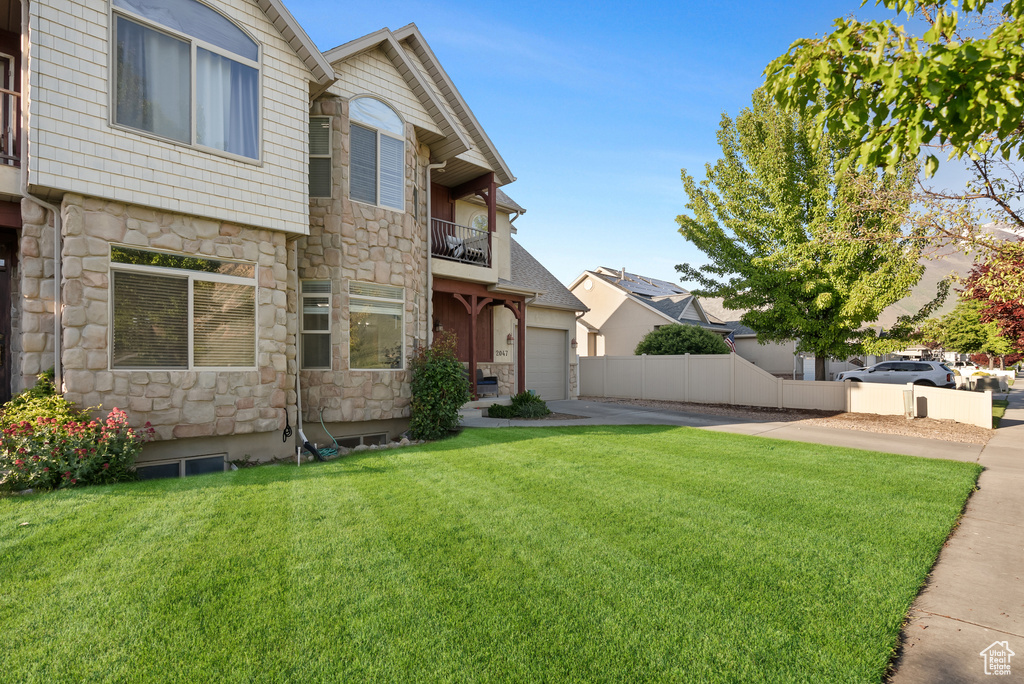 View of front of home featuring stone siding, a balcony, and concrete driveway