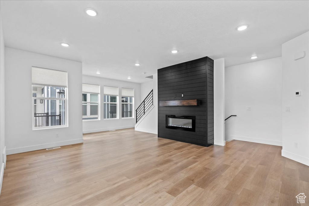 Unfurnished living room with baseboards, recessed lighting, light wood-style floors, a fireplace, and stairs