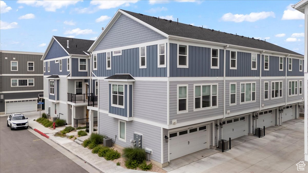 View of front facade with central AC unit, board and batten siding, concrete driveway, and a garage