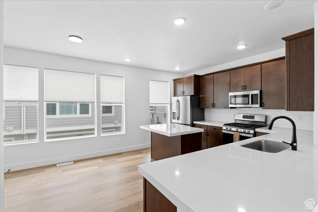 Kitchen featuring appliances with stainless steel finishes, a sink, dark brown cabinets, backsplash, and light countertops