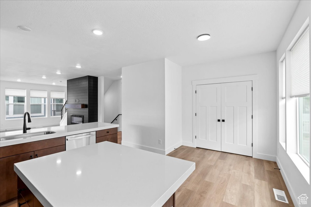 Kitchen with a sink, stainless steel dishwasher, light countertops, light wood-type flooring, and a kitchen island