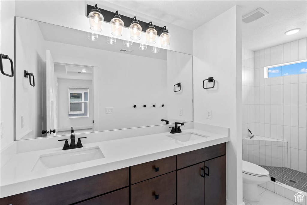 Full bath with toilet, double vanity, and a tile shower