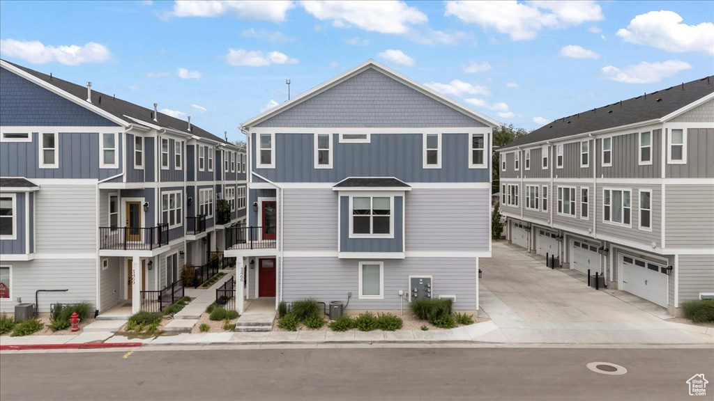 Townhome / multi-family property with driveway, a garage, cooling unit, and board and batten siding