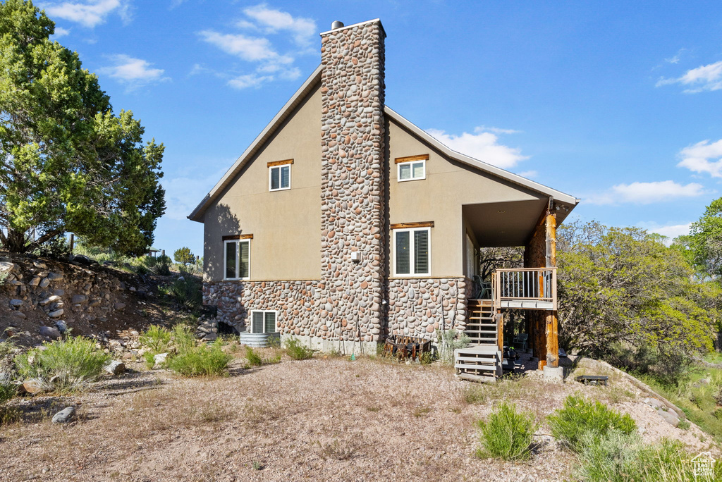 View of side of home featuring stone siding, stucco siding, a chimney, stairway, and central AC