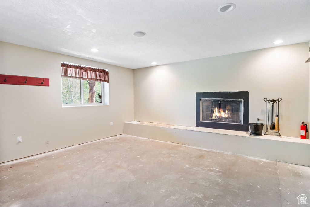Unfurnished living room with unfinished concrete flooring, recessed lighting, and a lit fireplace