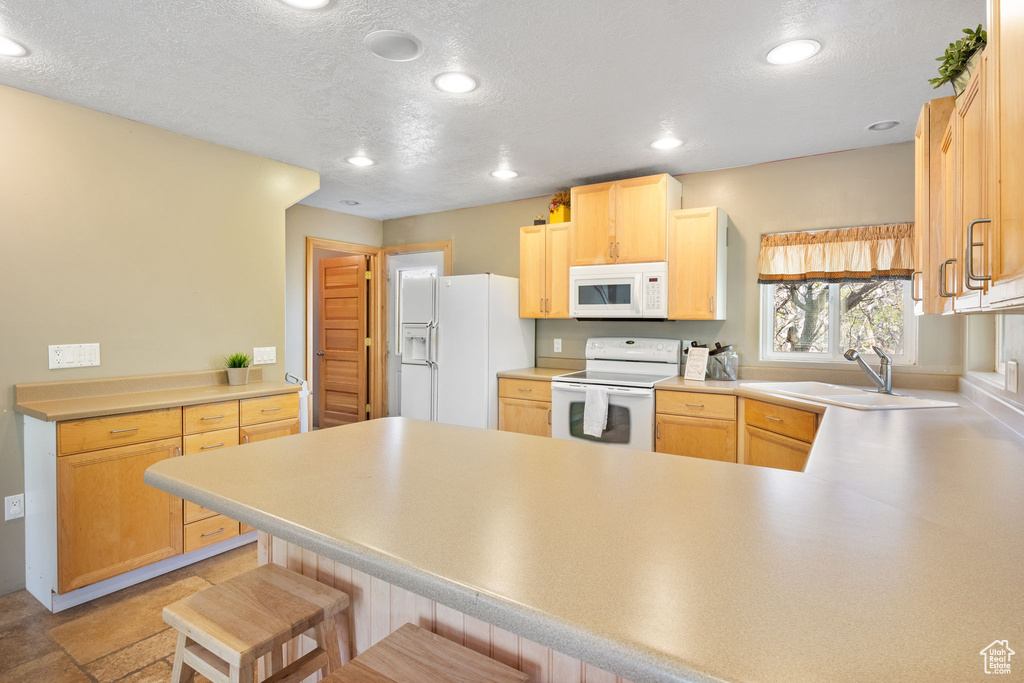 Kitchen featuring white appliances, a sink, a peninsula, light brown cabinets, and a textured ceiling
