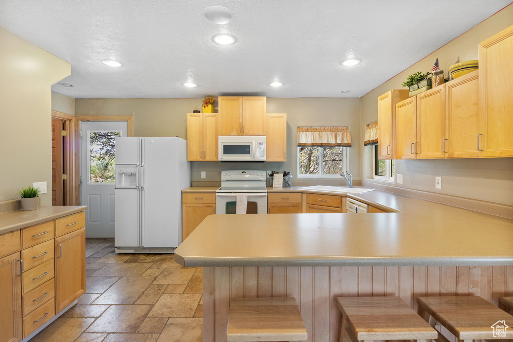 Kitchen featuring white appliances, a peninsula, a sink, recessed lighting, and stone tile floors