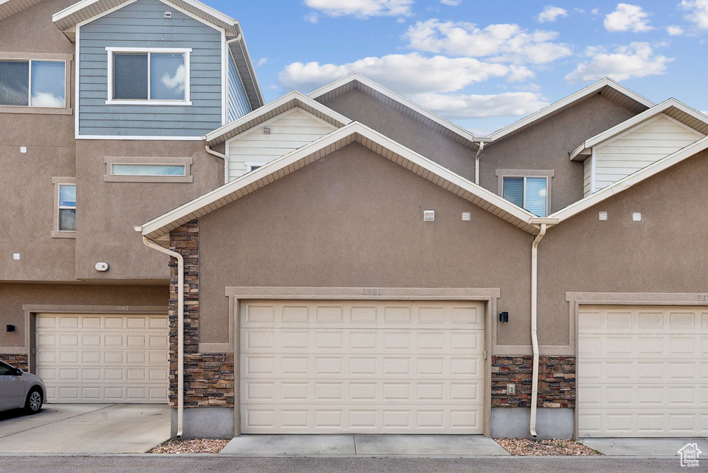 View of property with stone siding, stucco siding, and driveway
