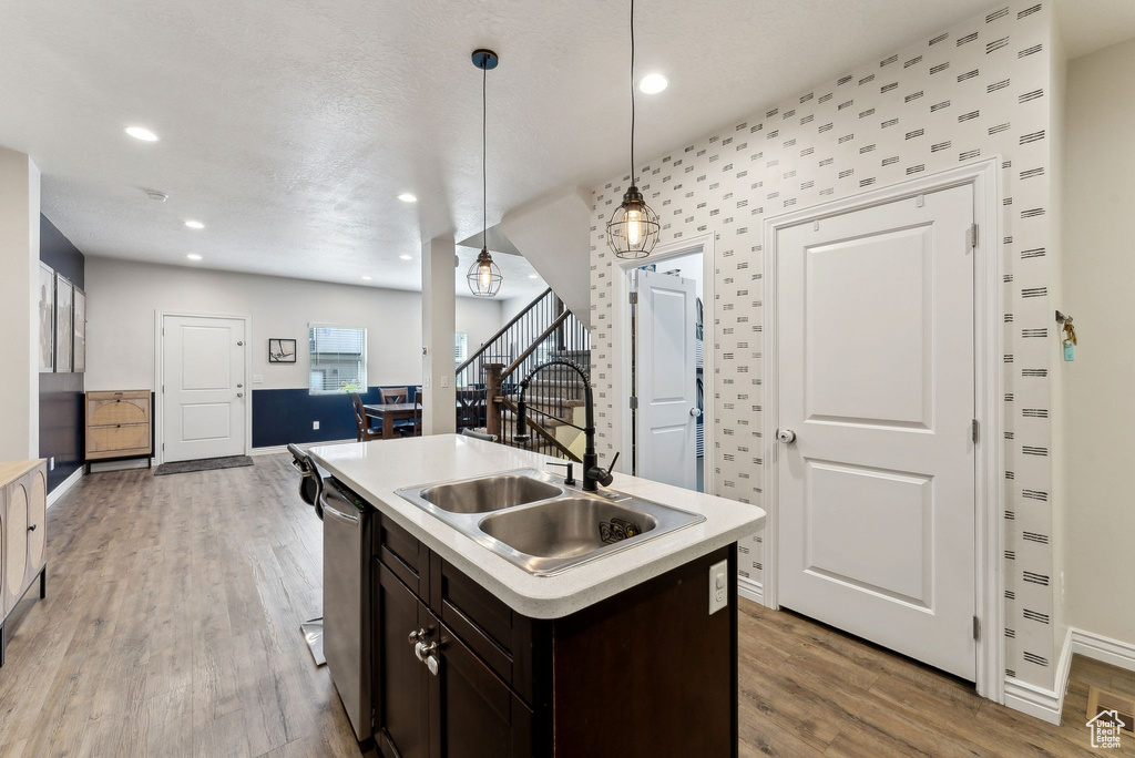 Kitchen featuring dishwasher, a sink, dark brown cabinets, light countertops, and light wood-style floors