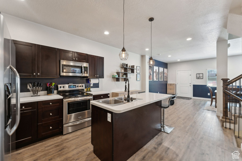 Kitchen featuring appliances with stainless steel finishes, a sink, a kitchen island with sink, light wood-style flooring, and recessed lighting