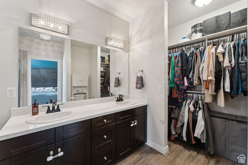 Full bathroom with double vanity, wood finished floors, a walk in closet, and baseboards