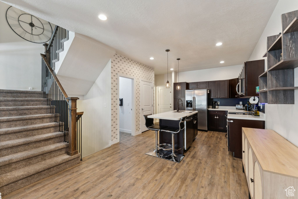 Kitchen with appliances with stainless steel finishes, a sink, light countertops, open shelves, and dark brown cabinetry