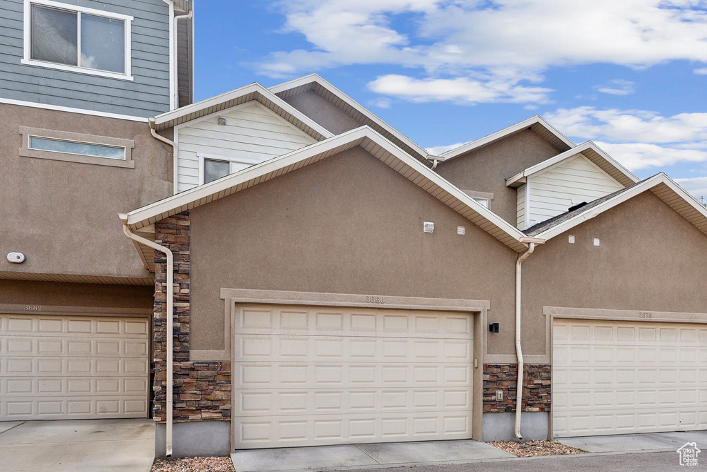 Townhome / multi-family property with stone siding, stucco siding, and an attached garage