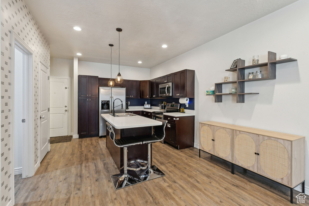 Kitchen with stainless steel appliances, light countertops, dark brown cabinetry, light wood finished floors, and a breakfast bar