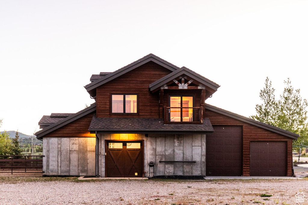 View of front of home featuring board and batten siding, a detached garage, roof with shingles, and gravel driveway