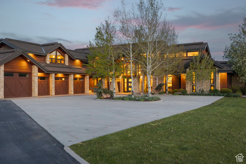 View of front of property with stone siding, driveway, and a yard