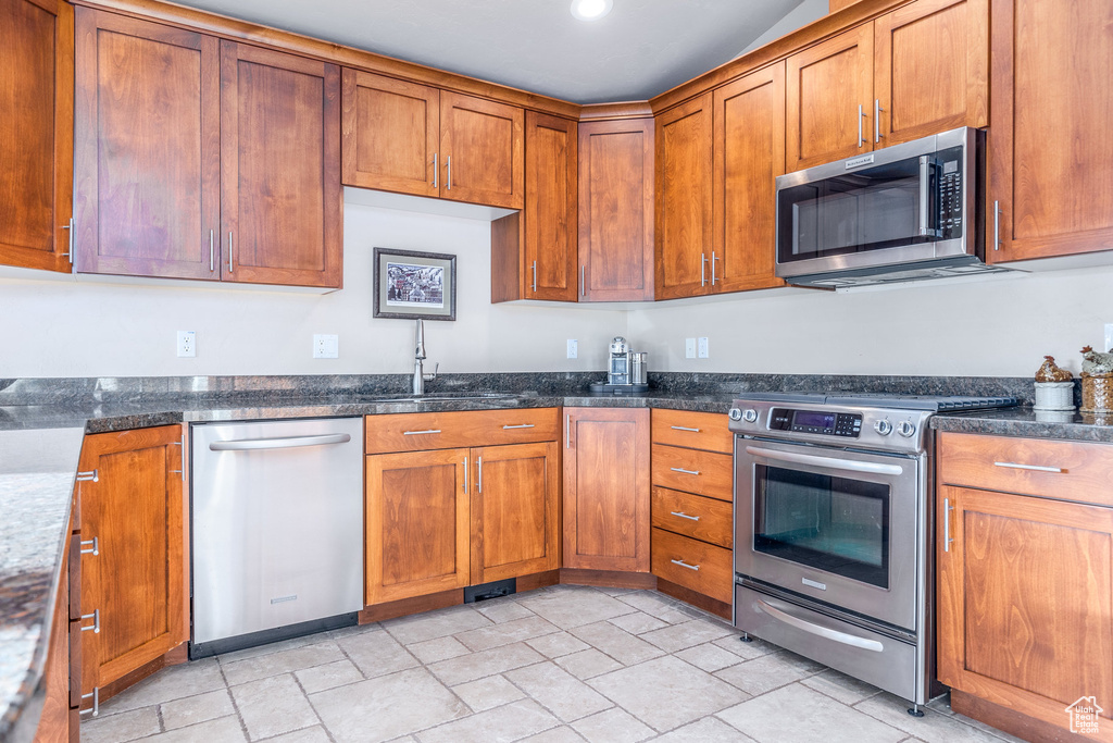 Kitchen featuring stainless steel appliances, a sink, brown cabinetry, dark stone counters, and recessed lighting