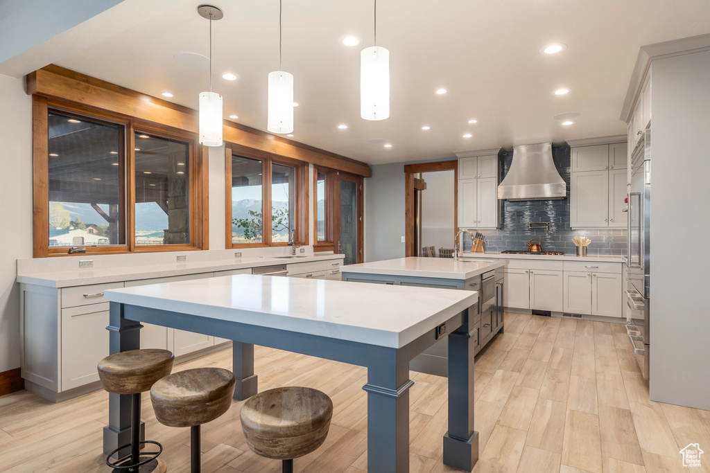Kitchen with extractor fan, a kitchen island with sink, tasteful backsplash, light wood-style flooring, and light countertops