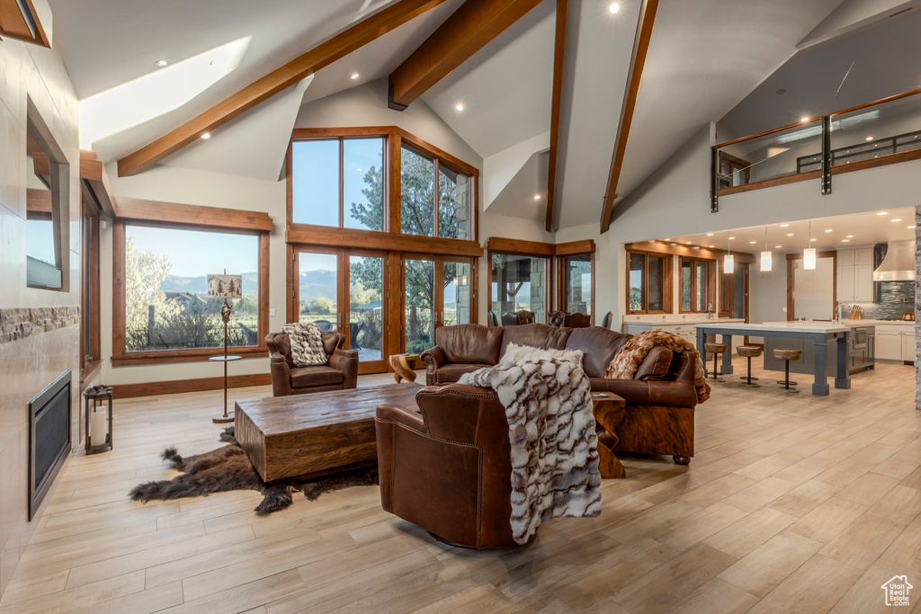 Living area with beamed ceiling, high vaulted ceiling, light wood-style floors, and a glass covered fireplace