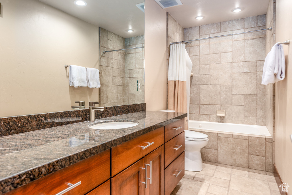 Full bathroom with vanity, toilet, tiled shower / bath combo, recessed lighting, and stone finish flooring