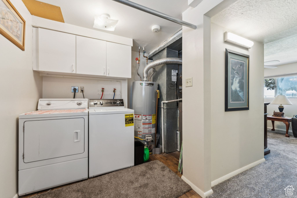 Laundry room featuring washing machine and dryer, water heater, cabinet space, baseboards, and a textured ceiling