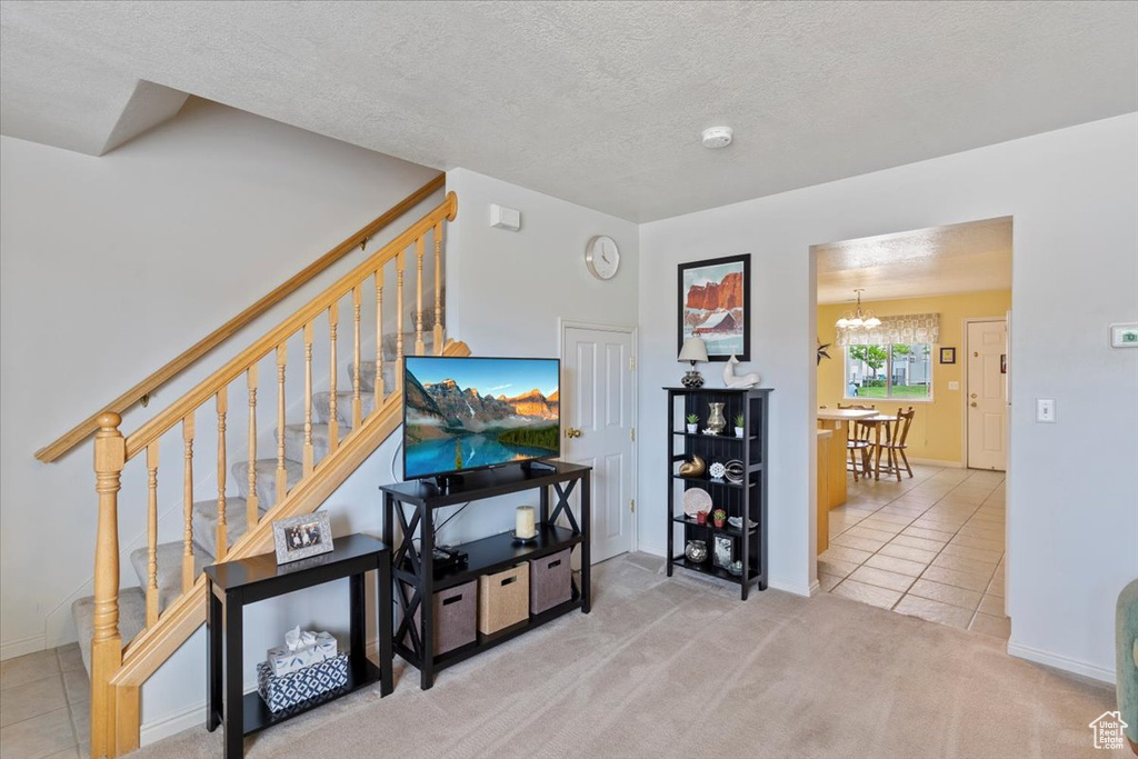 Tiled living room with stairs, a textured ceiling, a chandelier, carpet floors, and baseboards