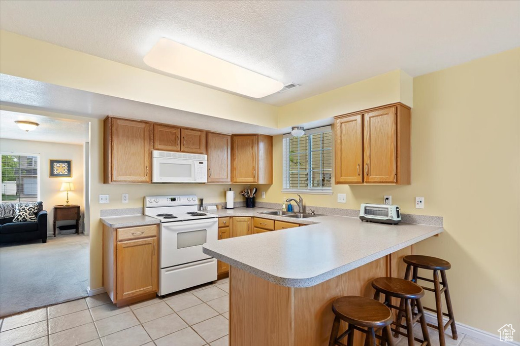 Kitchen with white appliances, a sink, a kitchen breakfast bar, a peninsula, and light countertops