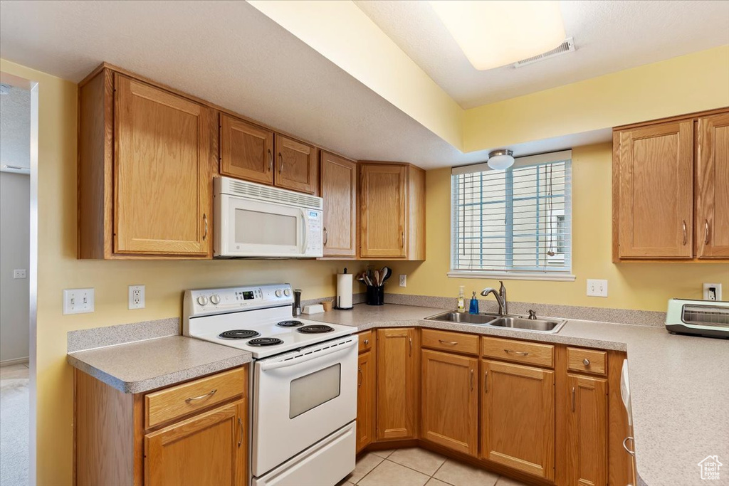 Kitchen with white appliances, a sink, light countertops, and light tile patterned floors