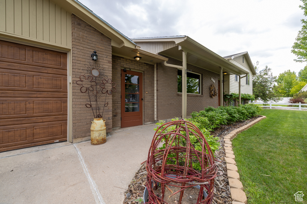 View of exterior entry featuring brick siding, a lawn, and an attached garage