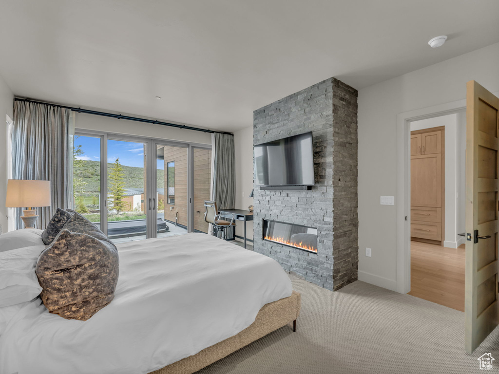 Bedroom with access to exterior, a stone fireplace, carpet flooring, and baseboards