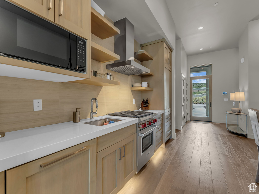 Kitchen featuring black microwave, wall chimney exhaust hood, luxury stove, open shelves, and a sink