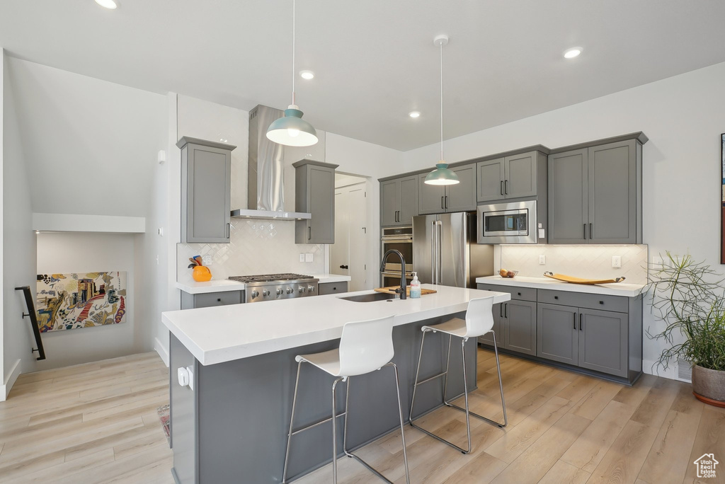 Kitchen featuring stainless steel appliances, gray cabinetry, wall chimney range hood, light wood-type flooring, and recessed lighting