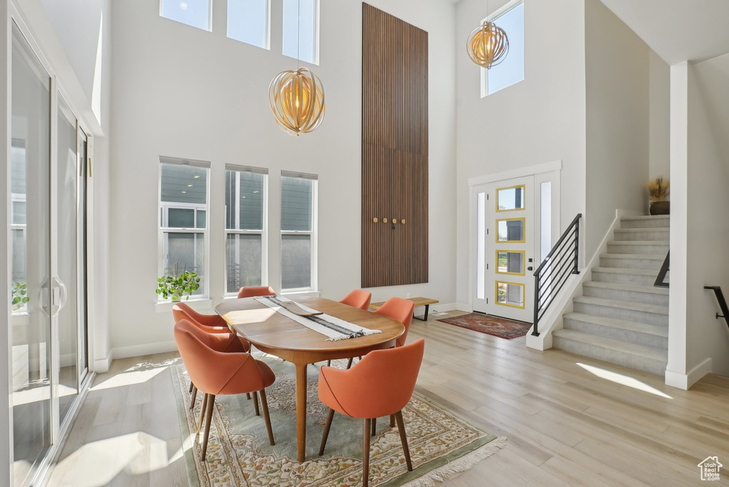 Dining area with a towering ceiling, light wood-style floors, stairs, a chandelier, and baseboards